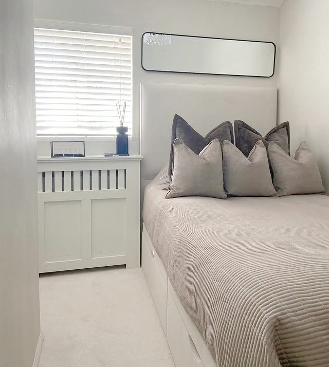 Small bedroom with a beige upholstered divan bed featuring storage drawers, styled with neutral bedding and accent cushions.